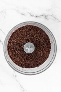 A food processor bowl filled with finely ground chocolate cookie crumbs.