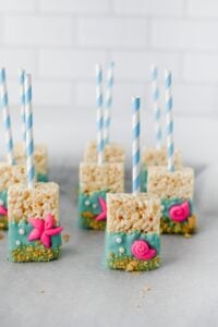 Rice Krispie treats on sticks, dipped in blue coating with pink sea-themed decorations.