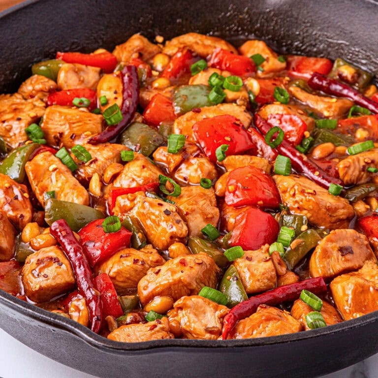 A skillet of kung pao chicken with peppers, peanuts, and green onions.