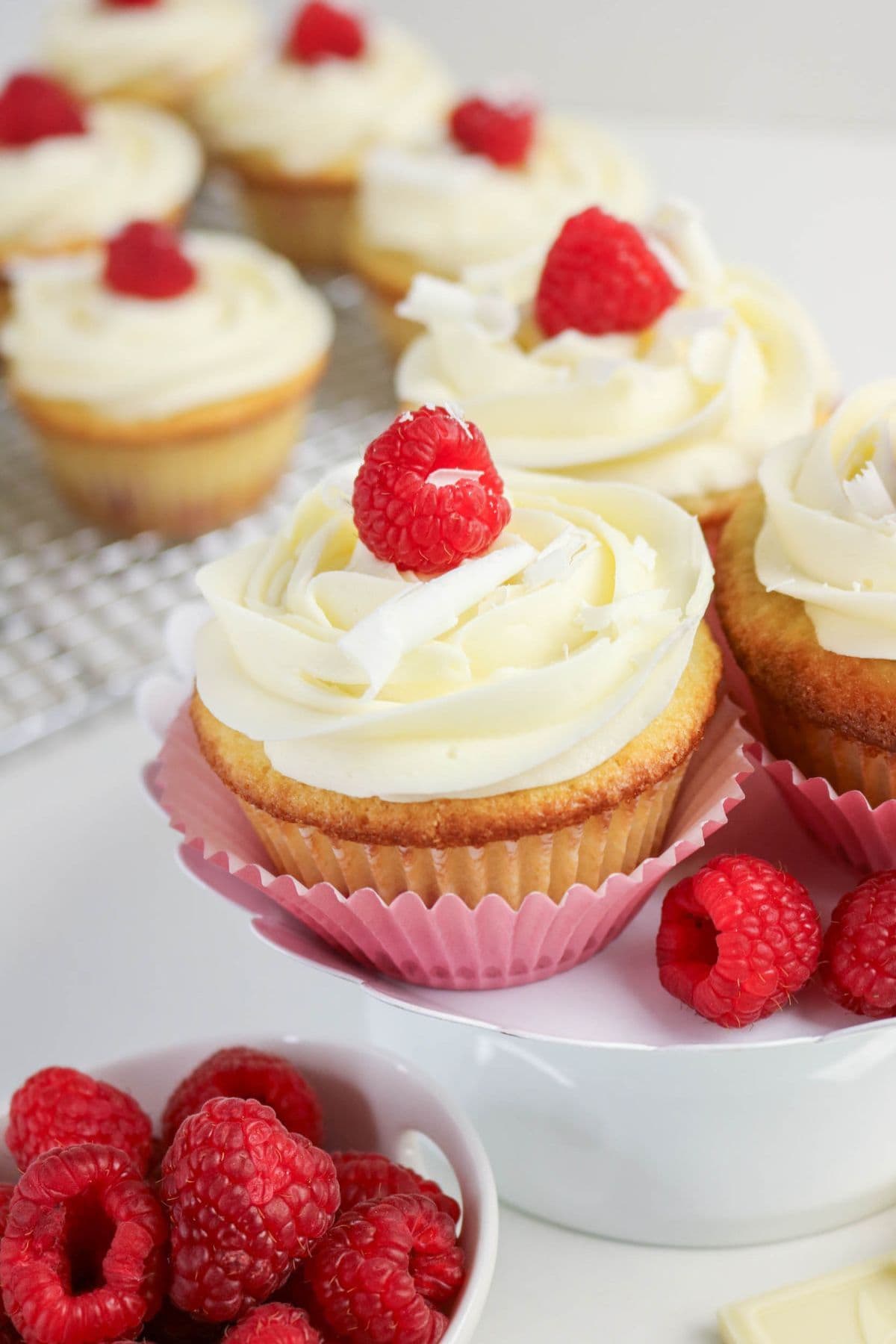 Vanilla cupcakes with white frosting, topped with raspberries—perfect for raspberry recipes.