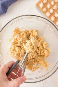 Hand holding a cookie scoop with dough over a bowl, with cookies on a tray.
