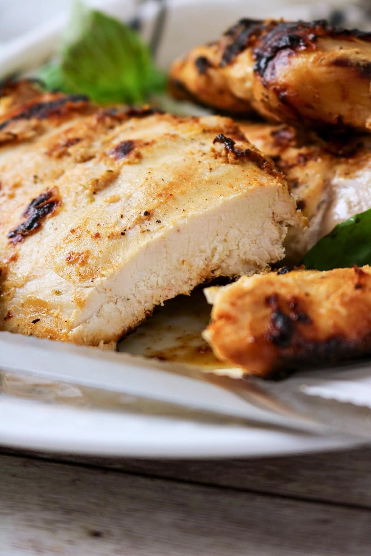 Grilled chicken breast sliced on a plate with grill marks and herbs.