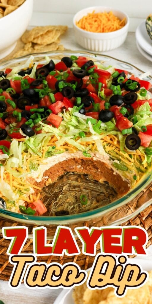 Glass dish of 7 layer taco dip topped with lettuce, cheese, tomatoes, and olives.