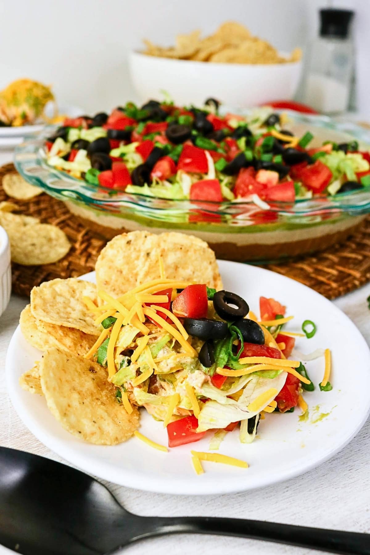 Tortilla chips with layered dip topped with cheese, olives, and vegetables.