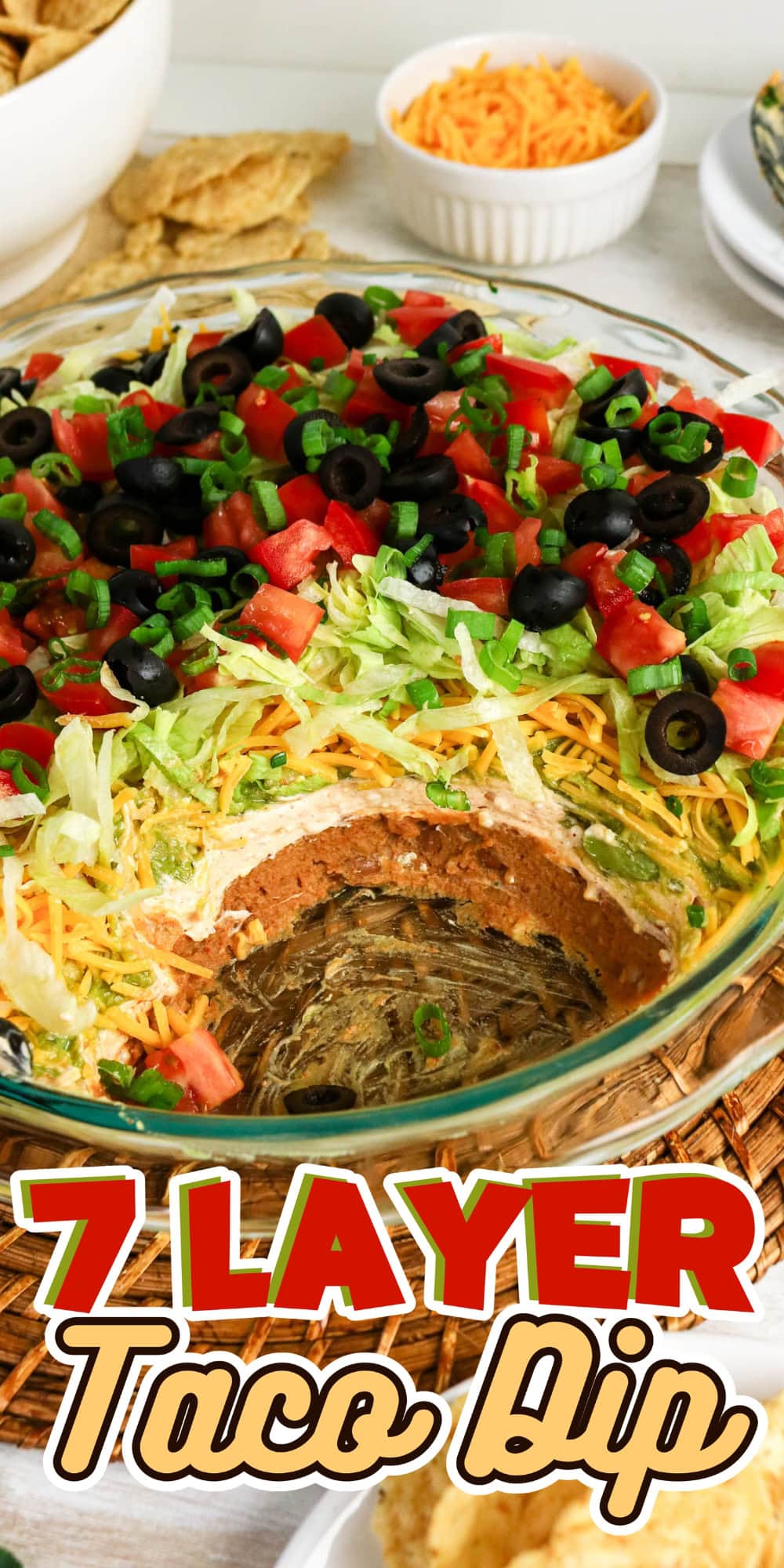 Glass dish of 7 layer taco dip topped with lettuce, cheese, tomatoes, and olives.