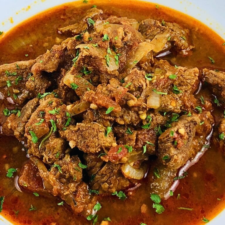 Beef curry in a rich, spicy red sauce garnished with chopped herbs.
