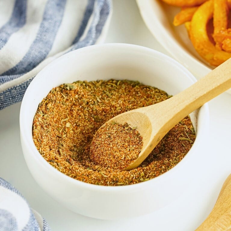 A bowl of seasoning mix with a wooden spoon next to curly fries.