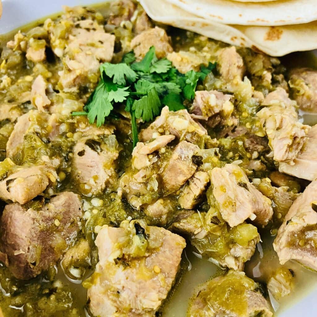Chunks of pork in green chili sauce, garnished with cilantro and served with tortillas.
