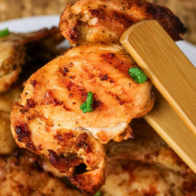 Grilled chicken thigh held by chopsticks, garnished with chopped green onions.