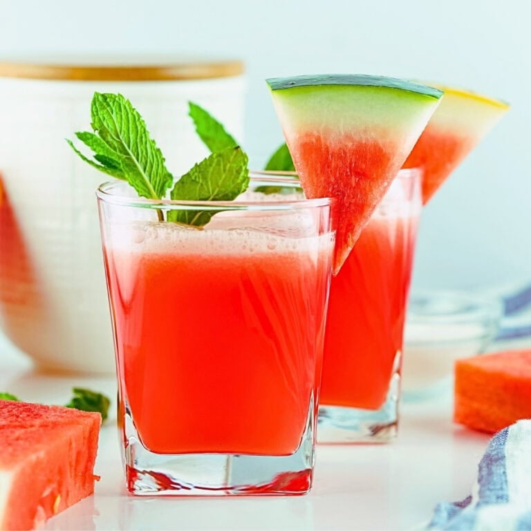 Two glasses of watermelon juice with mint and watermelon slices as garnish.