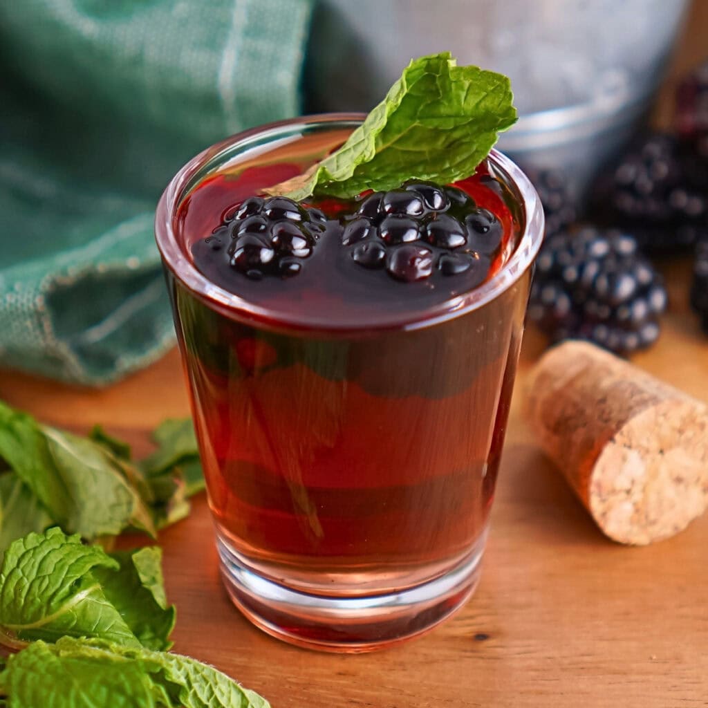 A glass of berry cocktail with mint garnish, blackberries, and a cork nearby.
