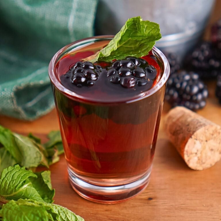 A glass of berry cocktail with mint garnish, blackberries, and a cork nearby.