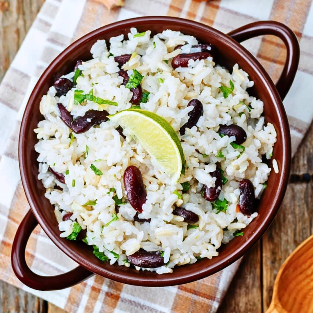 A bowl of rice and kidney beans garnished with cilantro and a lime wedge.