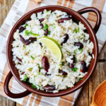 A bowl of rice and kidney beans garnished with cilantro and a lime wedge.