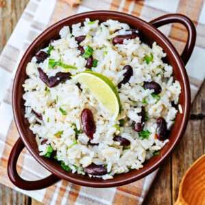 A bowl of rice and kidney beans garnished with cilantro and a lime wedge.