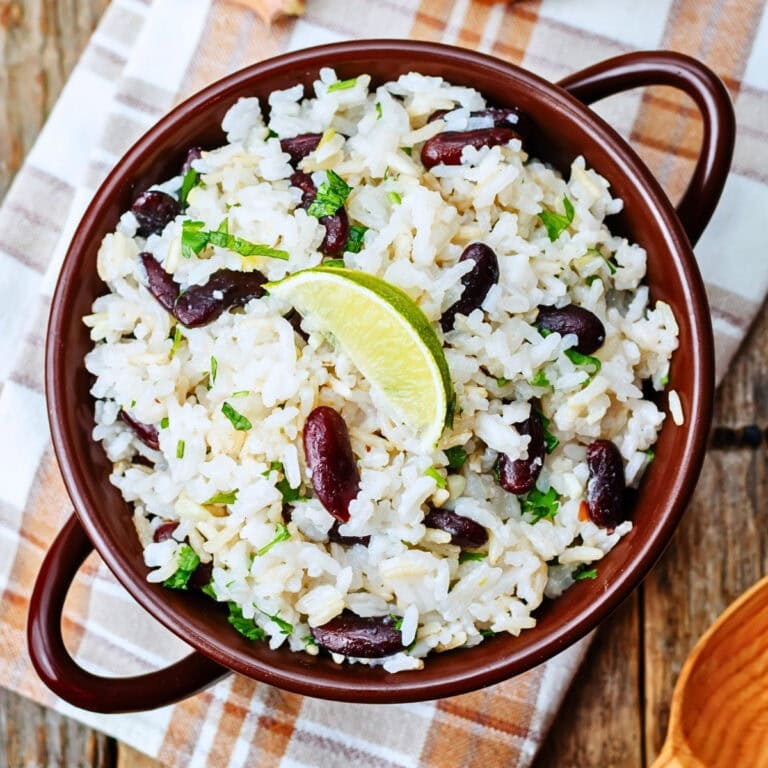 A bowl of rice and kidney beans garnished with cilantro and a lime wedge.