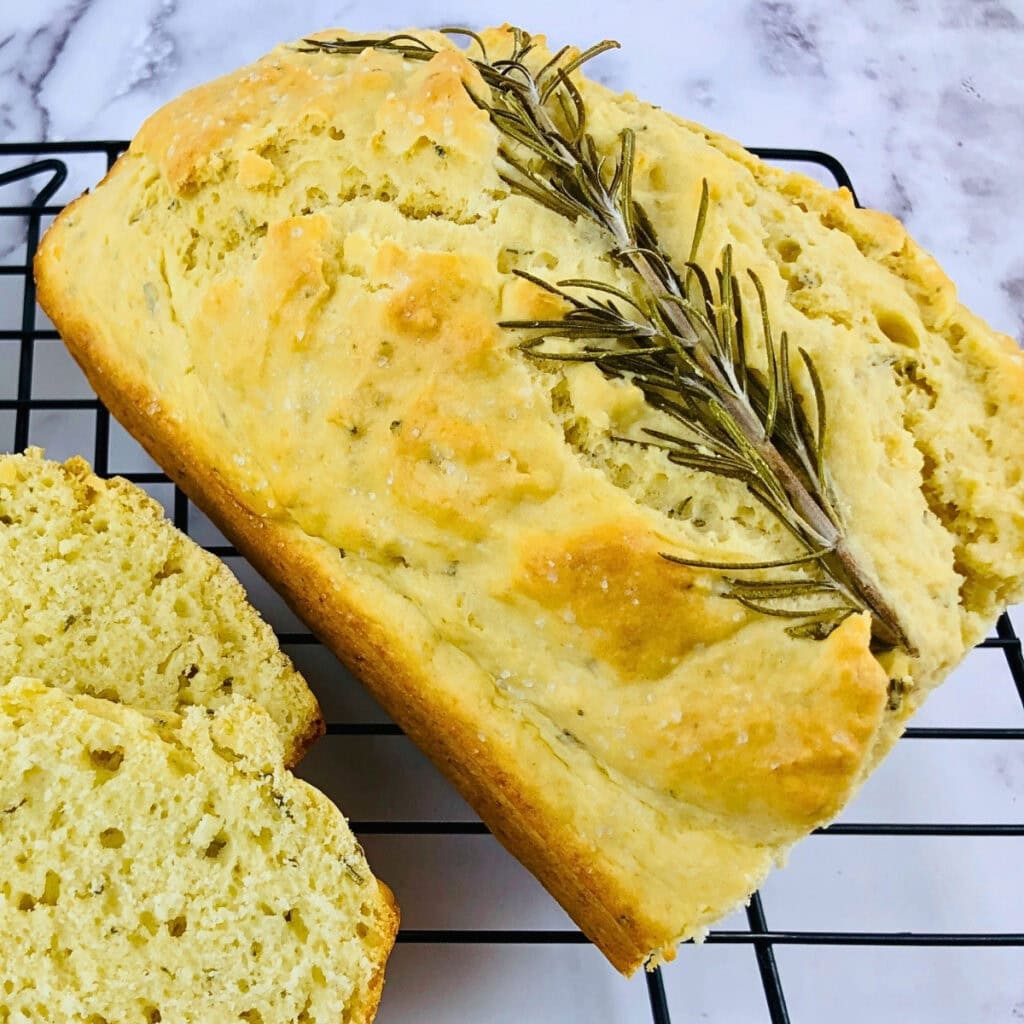 Loaf of rosemary bread with two slices, on a black cooling rack.