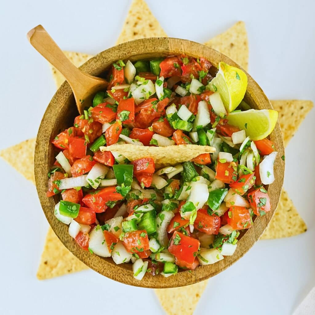 A wooden bowl of fresh salsa with tortilla chips and lime wedges, shot from above.