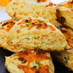 Cheese and chive scones stacked closely together on a dark surface.