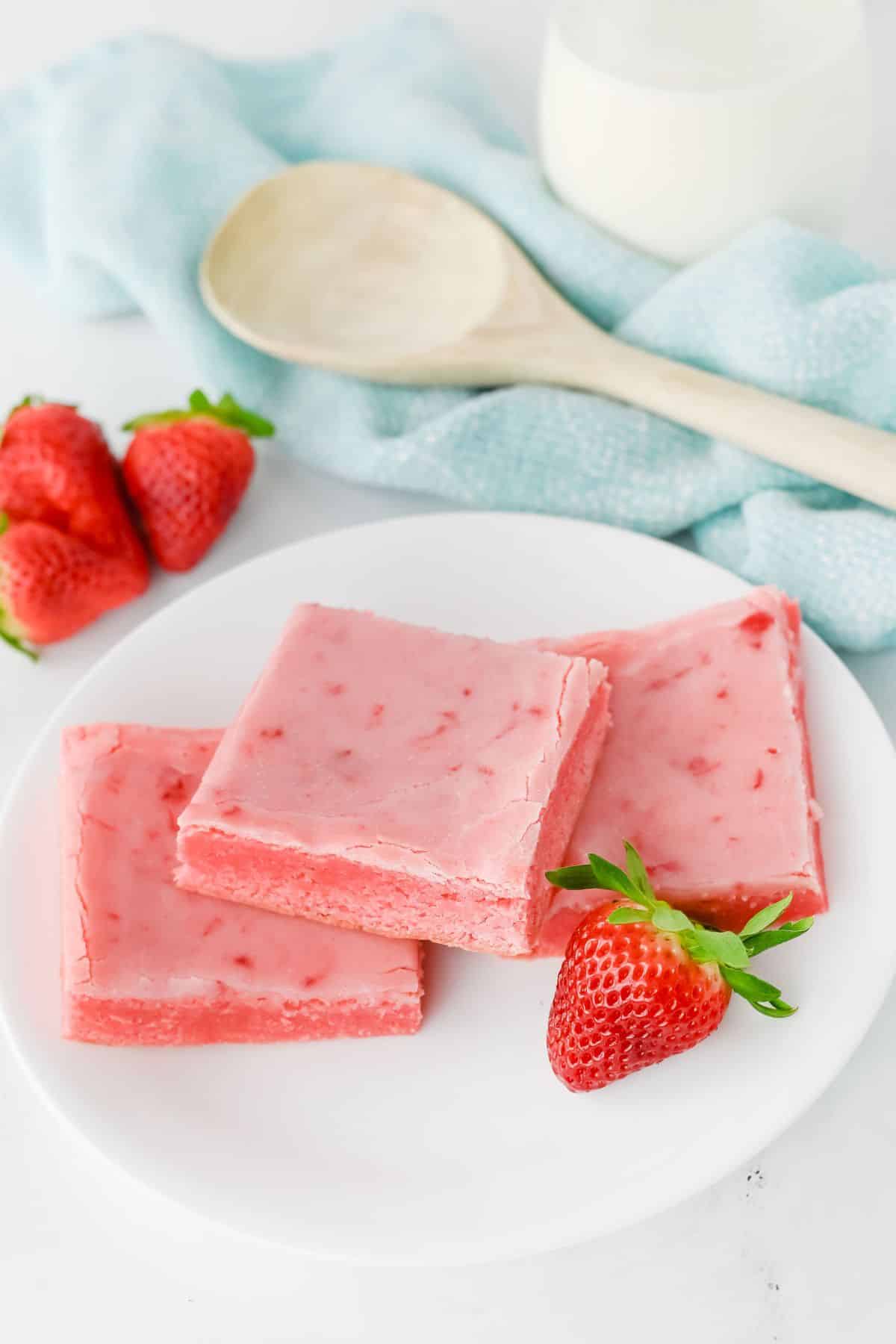 Three pink strawberry fudge squares and fresh strawberries on a white plate.