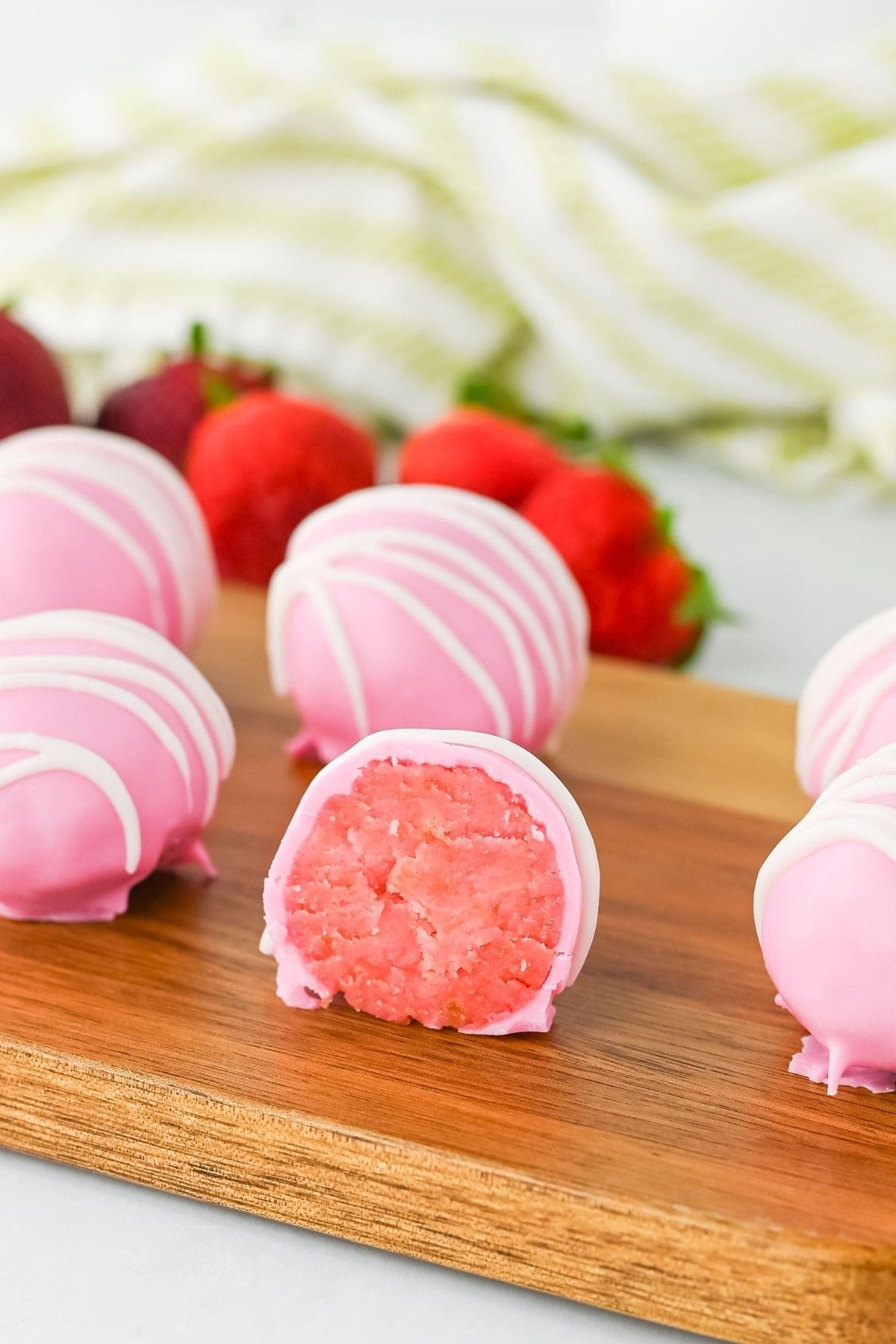Pink strawberry truffles with white drizzle, one cut open on a wooden board.