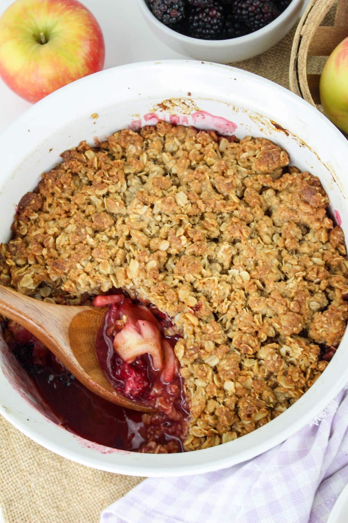 Apple and blackberry crumble with a wooden spoon in a white dish.