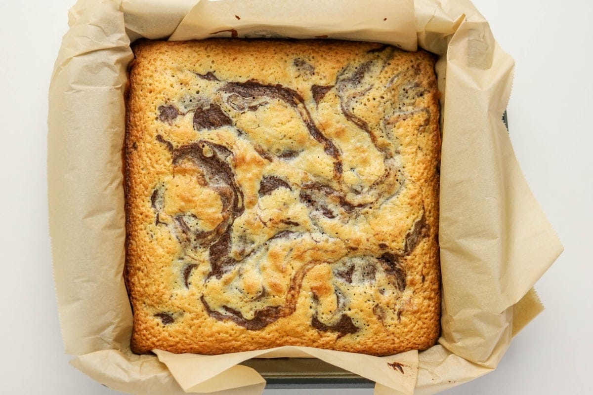 Marbled cake in a square pan lined with parchment paper, viewed from above.