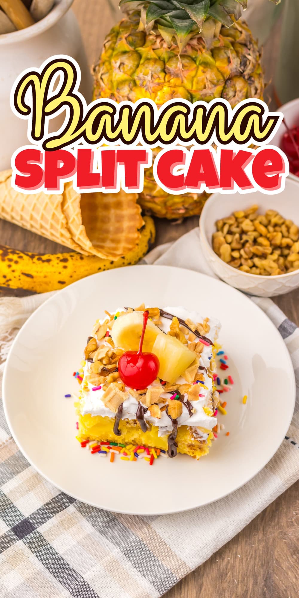 A slice of banana split cake with toppings and a cherry on a white plate.