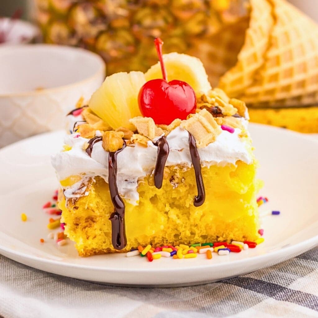 Slice of yellow cake with whipped topping, pineapple, cherry, and chocolate drizzle.