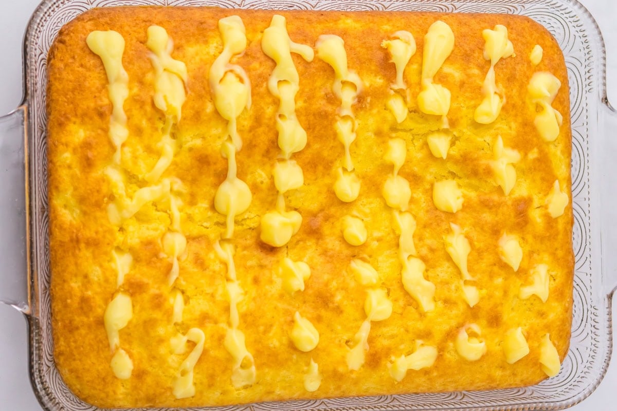 A rectangular yellow cake with drizzled yellow icing in a glass baking dish.