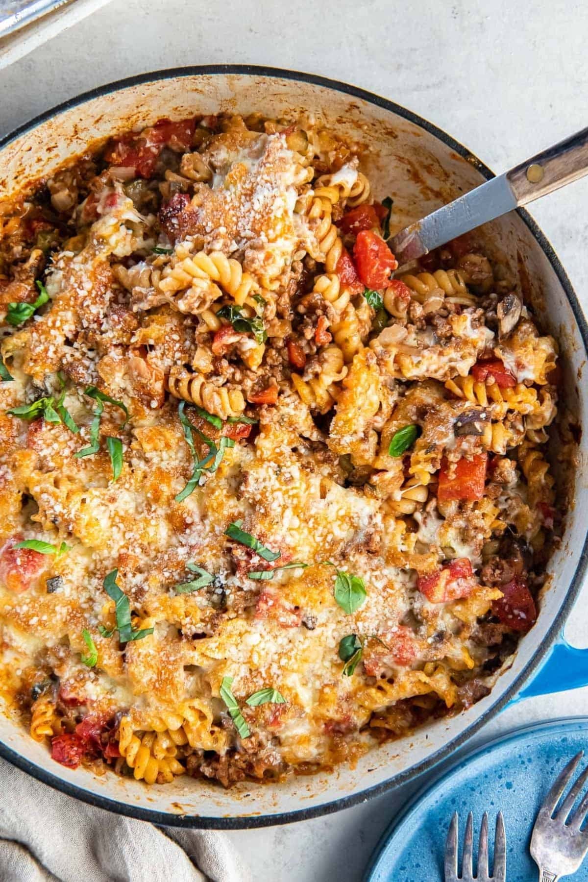 Baked pasta casserole with cheese, tomatoes, and herbs in a large skillet.