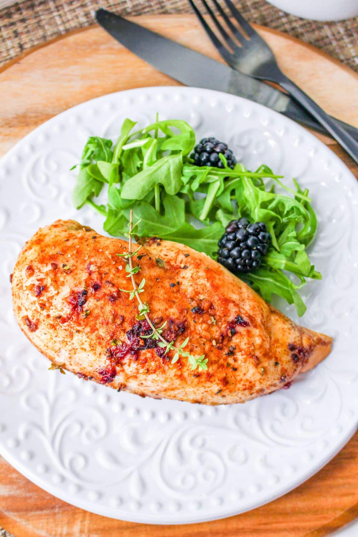 Grilled chicken breast with greens and blackberries on a white plate.