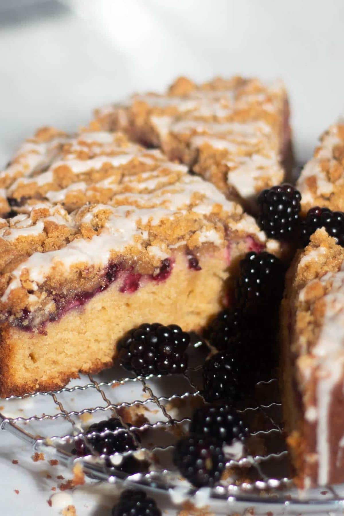 Slices of crumb-topped coffee cake with blackberries and white icing drizzle.