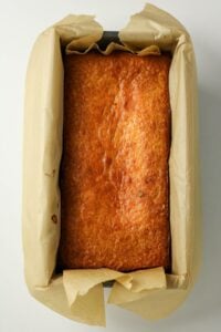 Golden loaf of cake in a parchment-lined rectangular baking tin, viewed from above.