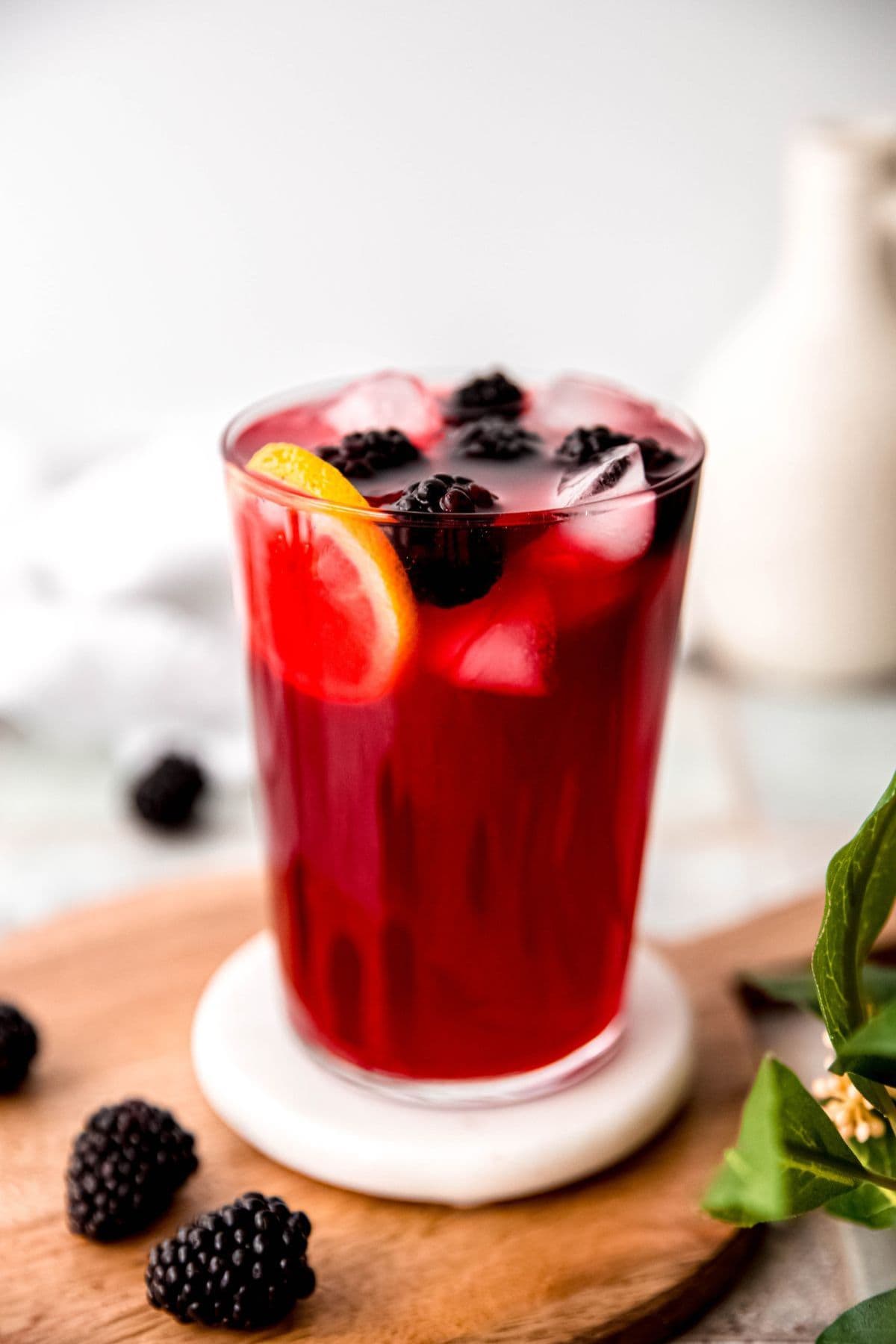 A glass of iced berry drink with lemon slice and blackberries on top.