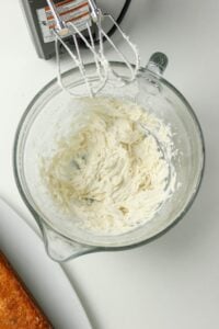 Glass bowl with whipped cream cheese frosting and electric mixer beaters above.
