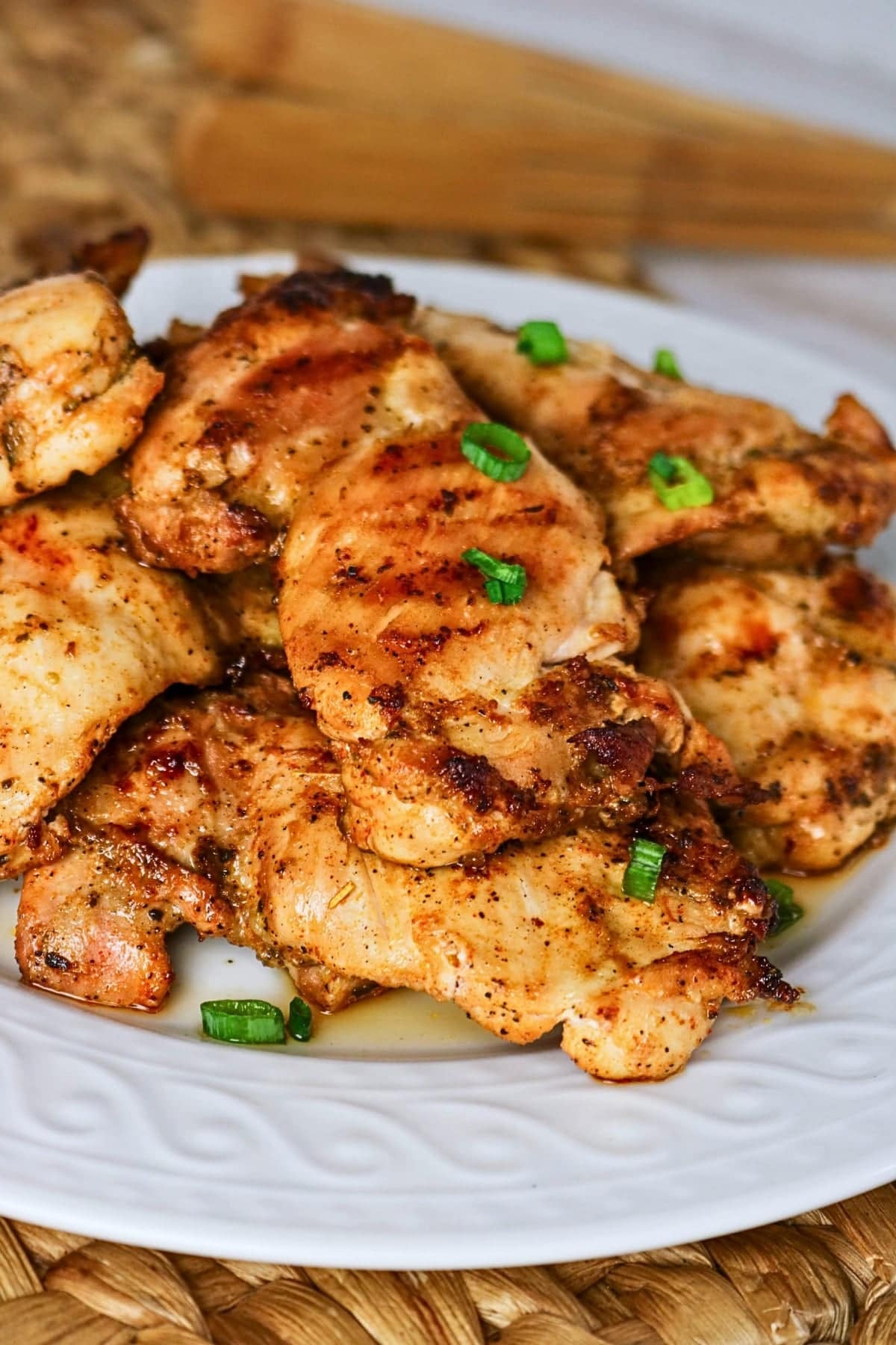 Grilled chicken pieces garnished with chopped green onions on a white plate.