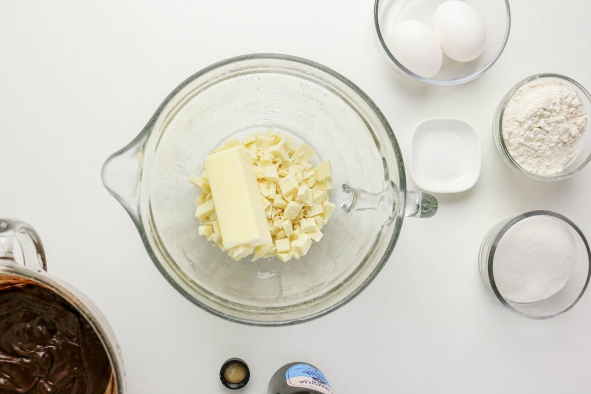 Top view of baking ingredients: butter, eggs, flour, sugar, and chocolate in bowls.