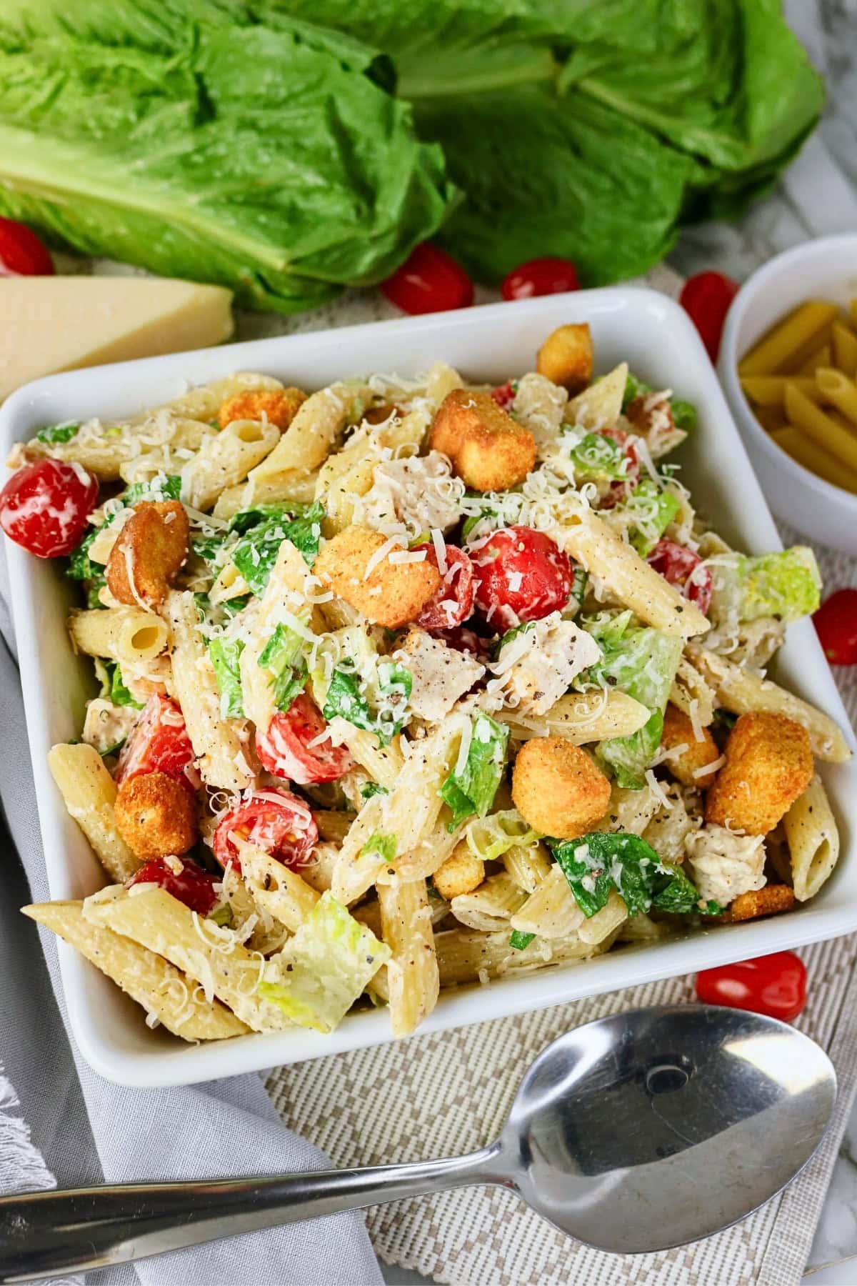 Pasta salad with lettuce, cherry tomatoes, croutons, and grated cheese in a bowl.