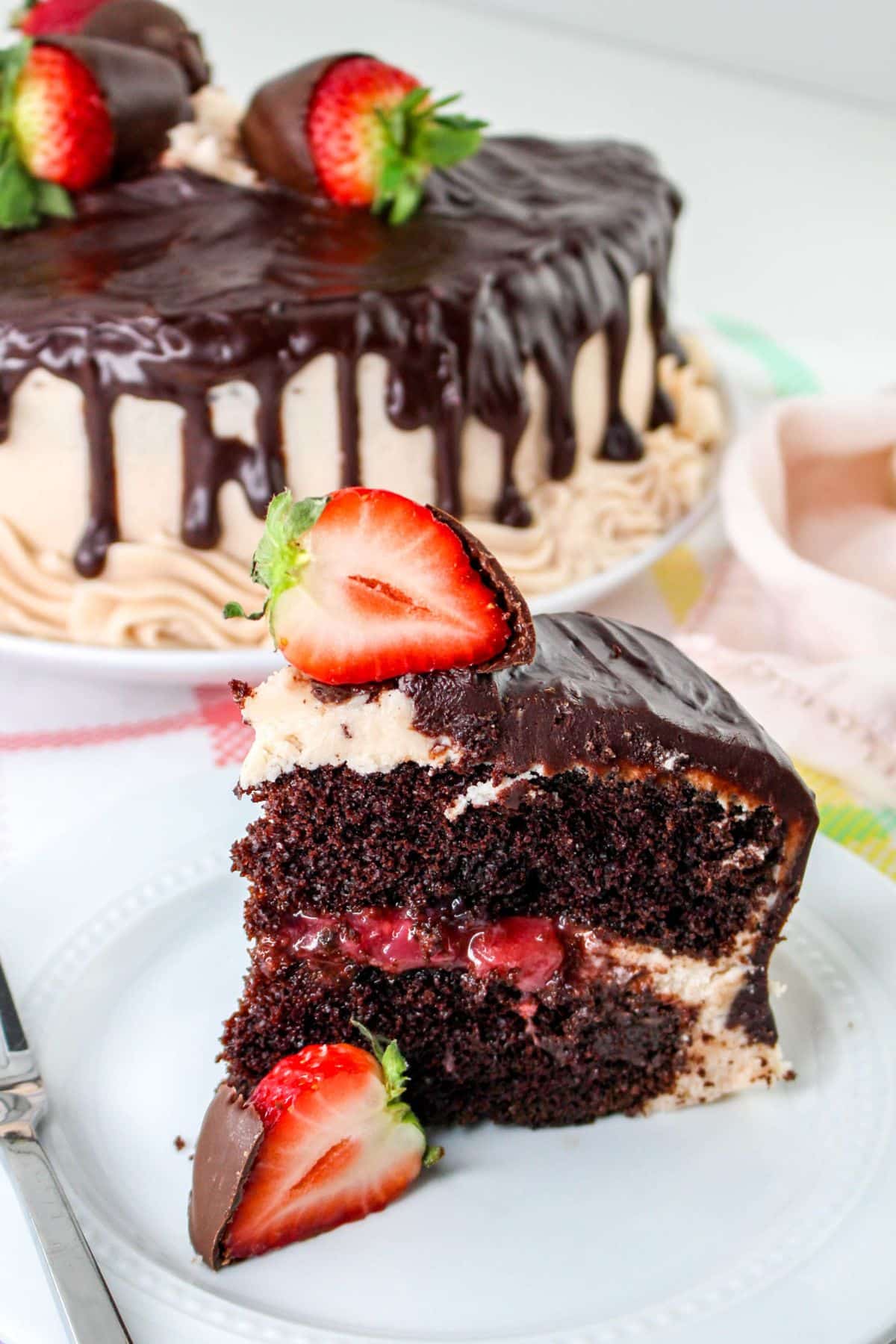 A slice of chocolate cake with strawberries and chocolate ganache on a white plate.