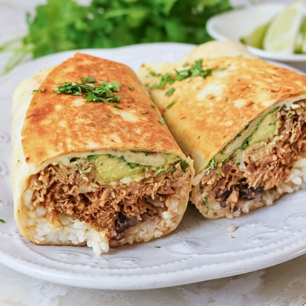 Two burrito halves on a white plate, filled with rice, meat, and avocado.