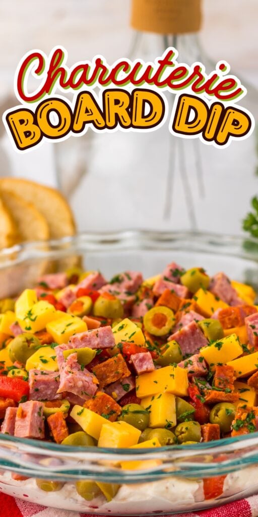 A glass bowl of charcuterie board dip with meats, cheese, and olives on top.
