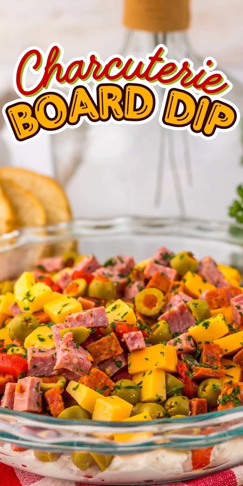 A glass bowl of charcuterie board dip with meats, cheese, and olives on top.