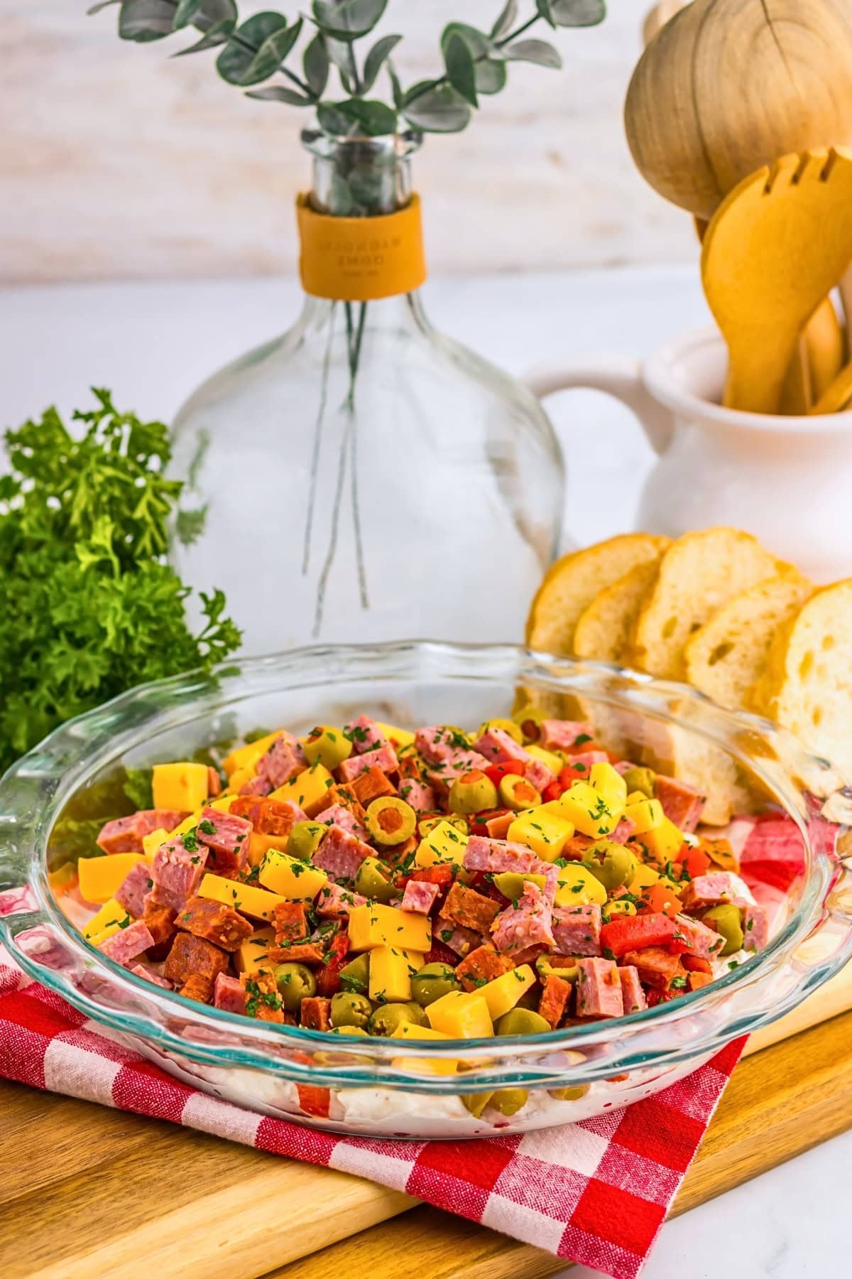 A glass dish of chopped salad with cheese, meats, and olives on a red napkin.