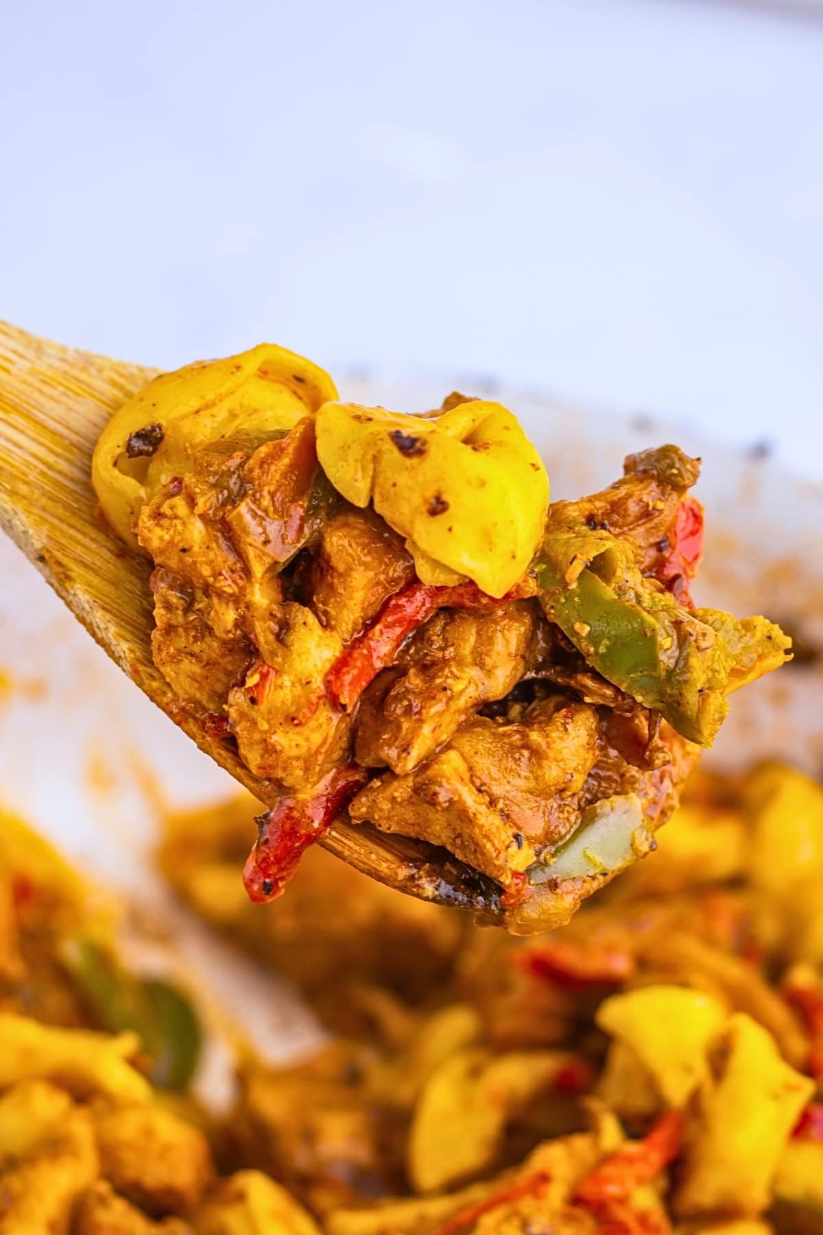 A wooden spoon holds pasta with vegetables and a creamy, spiced sauce.