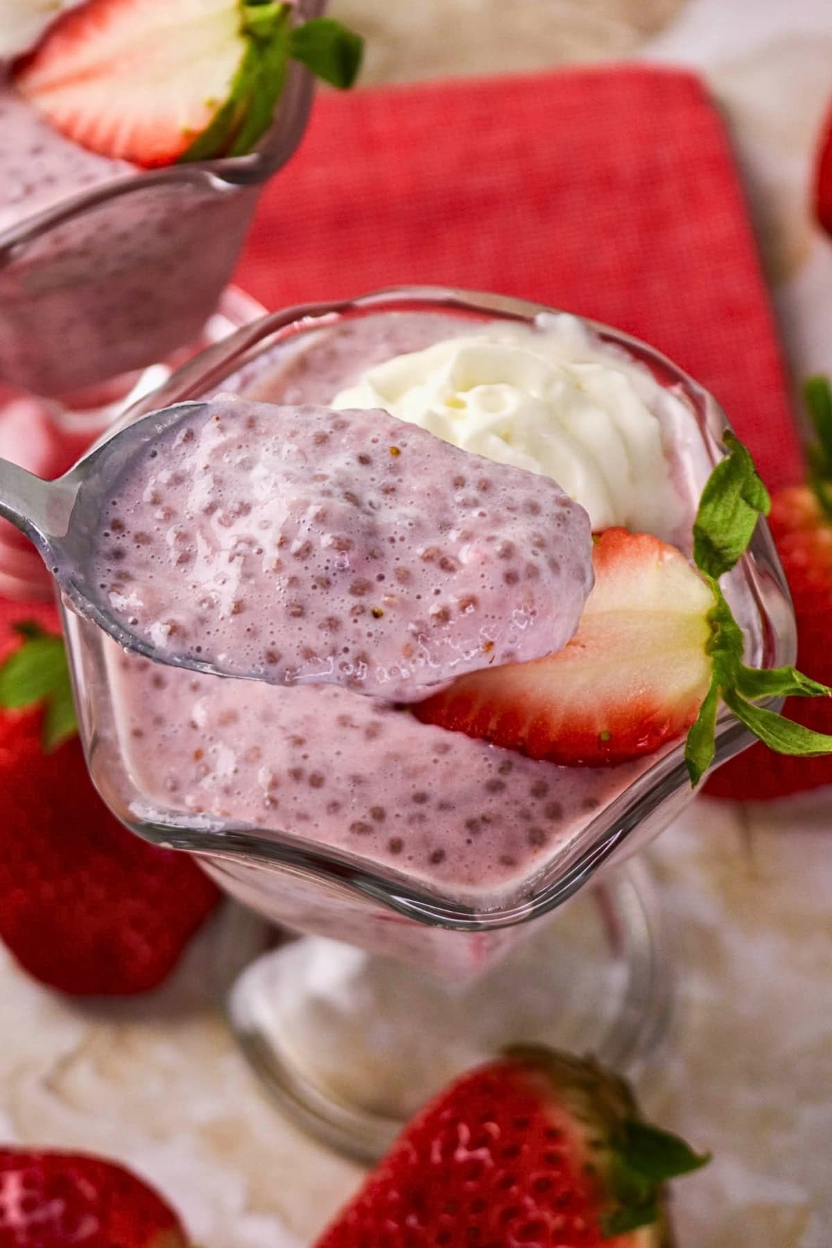 A spoonful of strawberry chia pudding in a glass, topped with cream and a strawberry.