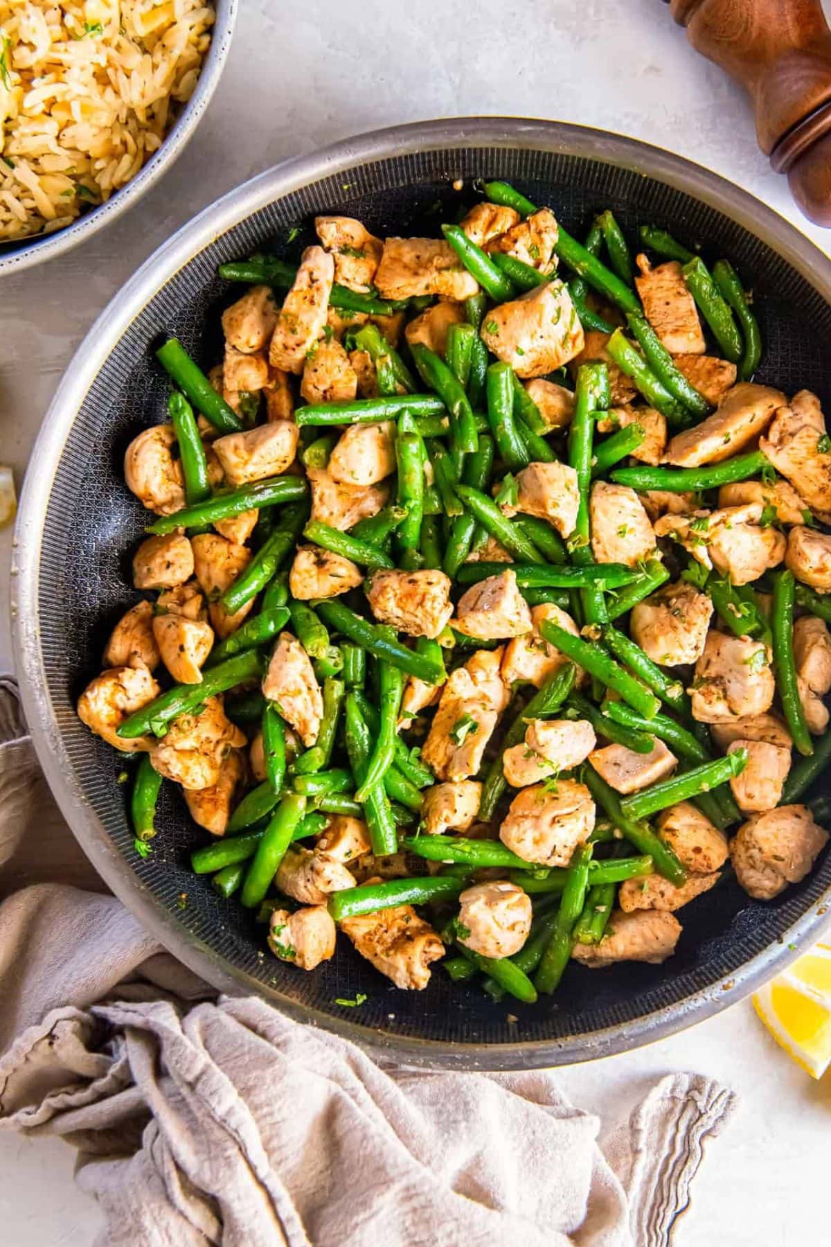 Skillet with cooked chicken pieces and green beans on a light table.