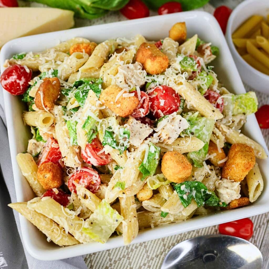 Pasta salad with cherry tomatoes, lettuce, croutons, and grated cheese in a bowl.