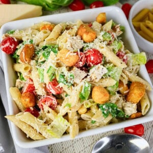 Pasta salad with cherry tomatoes, lettuce, croutons, and grated cheese in a bowl.