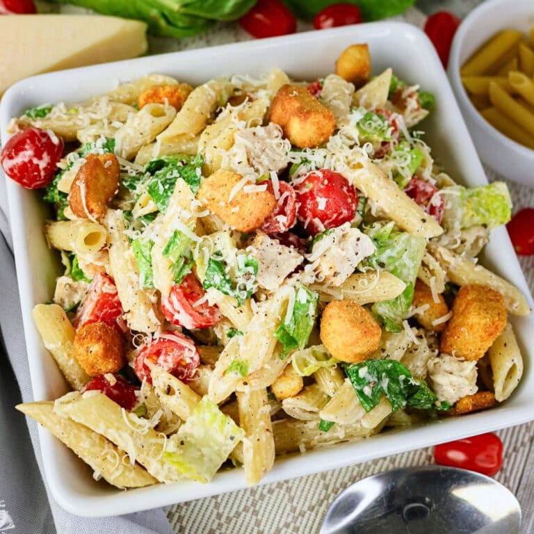 Pasta salad with cherry tomatoes, lettuce, croutons, and grated cheese in a bowl.